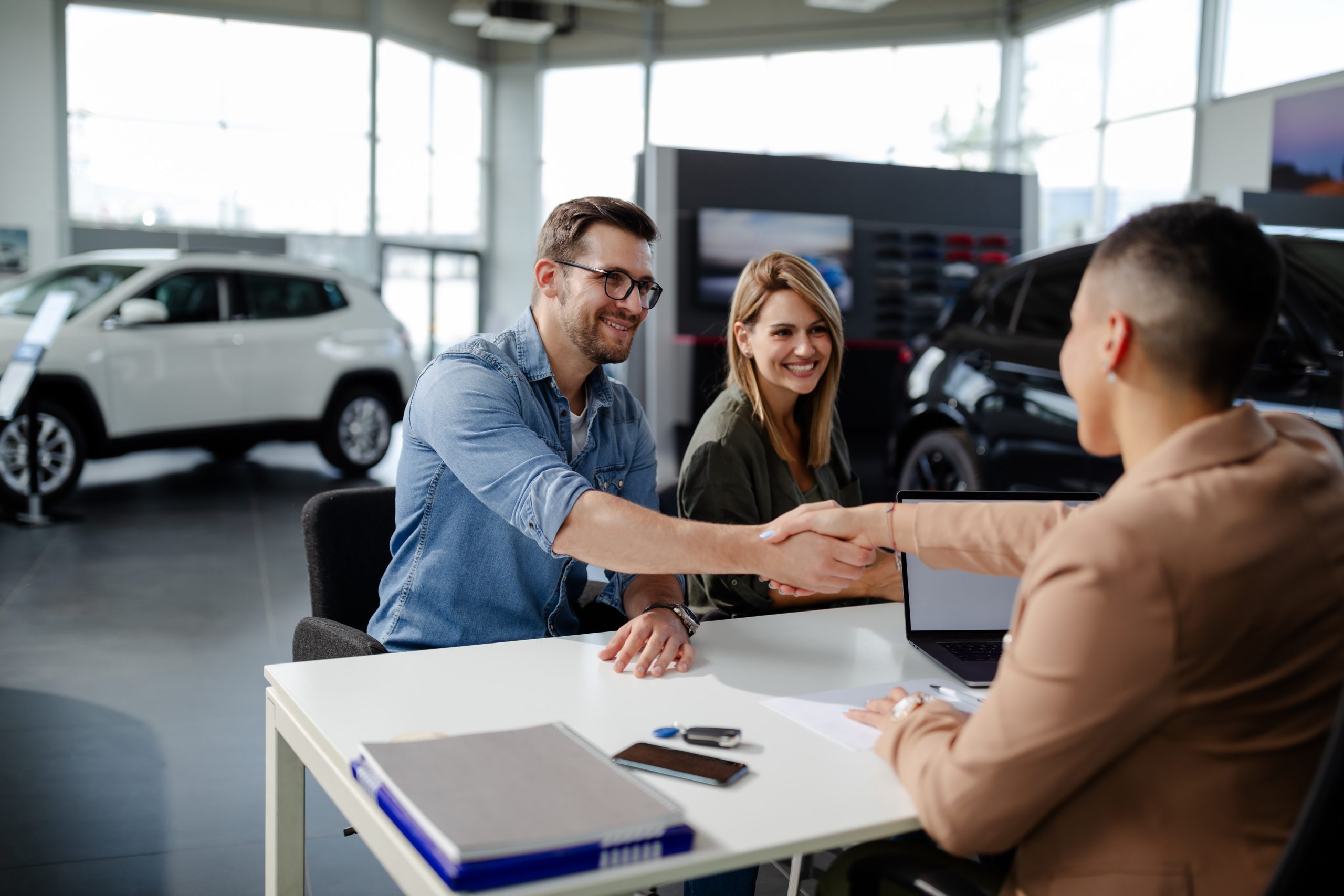 A couple shakes hands at the dealership after getting all of their auto loan questions answered.